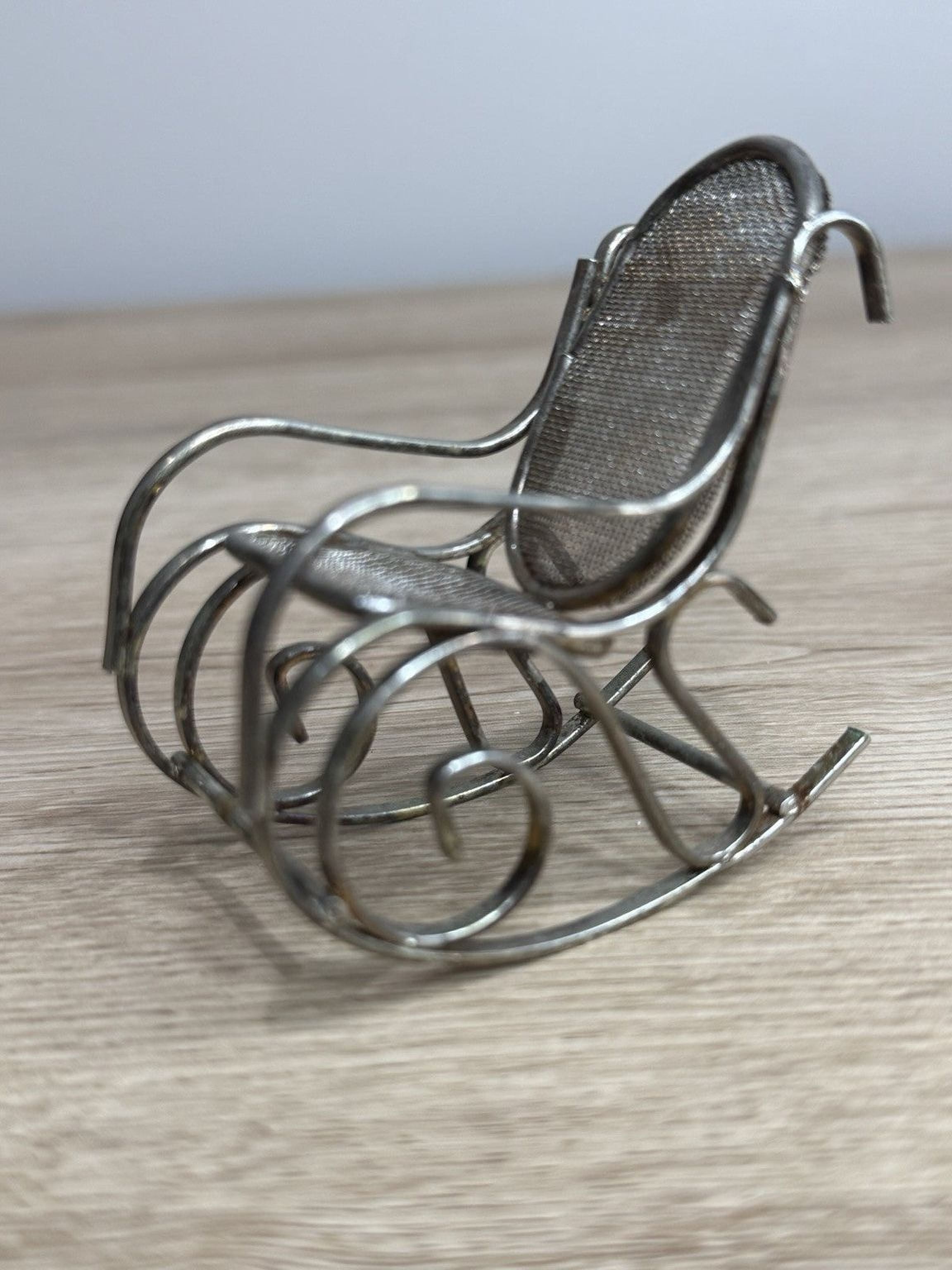 A small, metal rocking chair with a wire mesh backrest sits on a wooden surface.