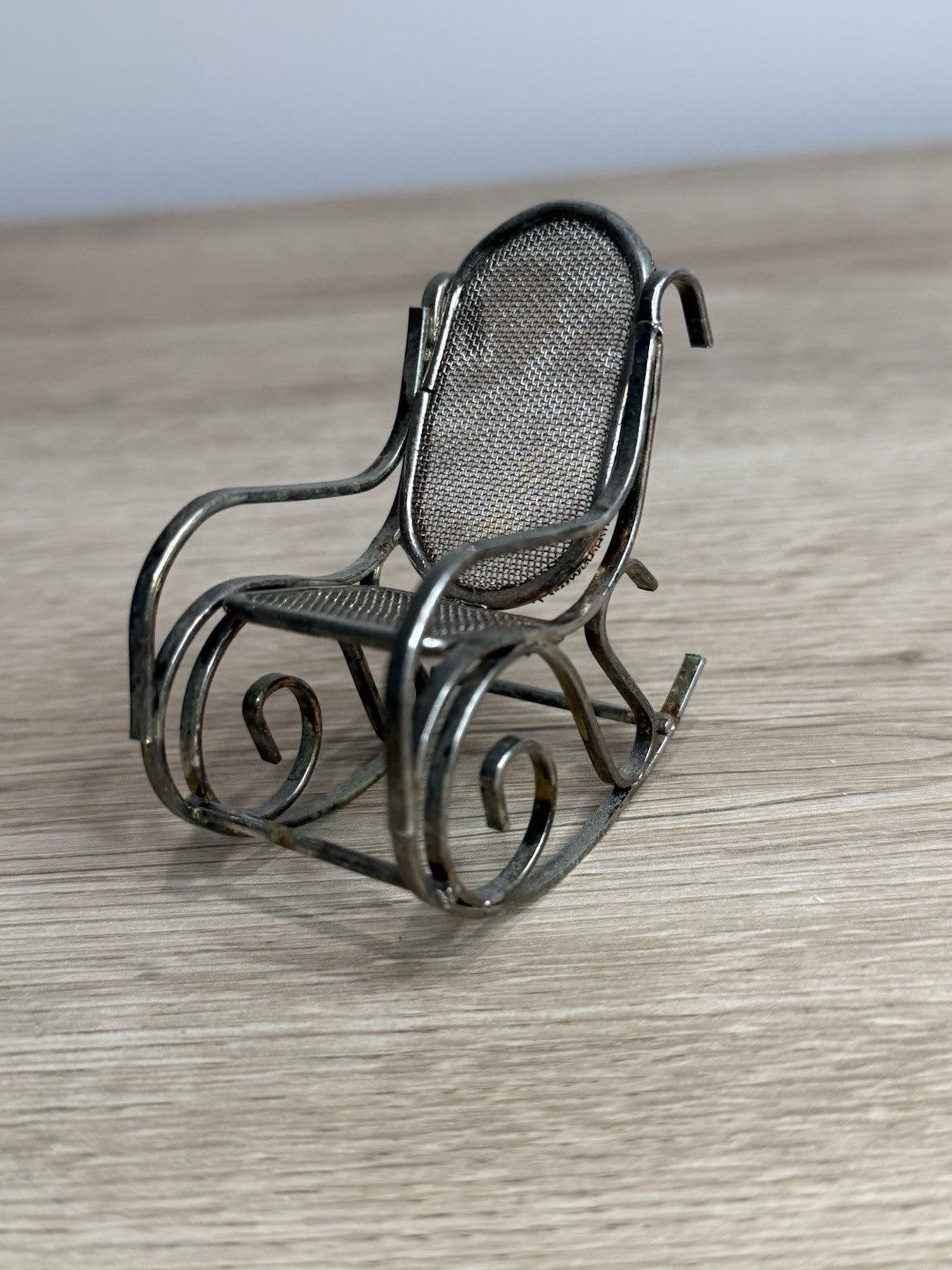 A small, metal rocking chair with a mesh backrest sits on a wooden surface.